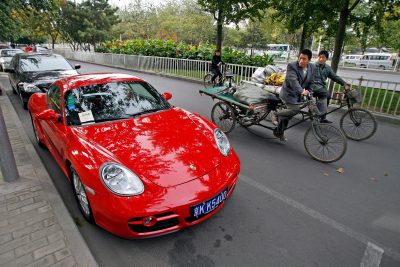 Two men carrying goods to be recycled ride their flatbed tricycles past a red Porsche Cayman parked outside a high-end housing complex in Beijing, China. (Photo: AAP).