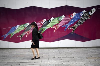 A woman walks near a wall painting featuring traditional carp streamers in Tokyo, 3 May 2016. (Photo: AP Photo/Eugene Hoshiko).