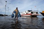 A man carrying empty bottles of mineral water walks through water at the Muara Angke port, that floods due to the high tides, in Jakarta, Indonesia, 9 November, 2021 (Photo: Reuters/Willy Kurniawan).