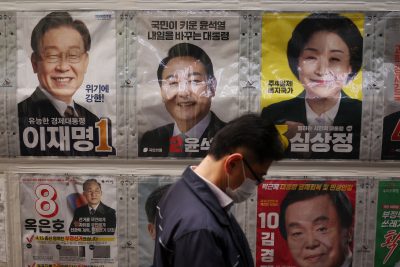 A man stands in front of posters of candidates for the upcoming March 9 presidential election as he queues to cast his early vote at a polling station in Seoul, South Korea, 4 March 2022. Reuters/Kim Hong-Ji