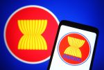 The ASEAN emblem is seen on a smartphone screen in front of the ASEAN flag. (Photo: Pavlo Gonchar/Reuters)