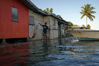 El niño local Ratusila Wakanaseva, de 14 años, vadea agua de mar torrencial sobre un malecón ineficaz durante la marea alta, mientras la comunidad local sufre inundaciones en el pueblo de Sirwa, Fiji, el 15 de julio de 2022 (Foto: REUTERS/Lauren Elliott).